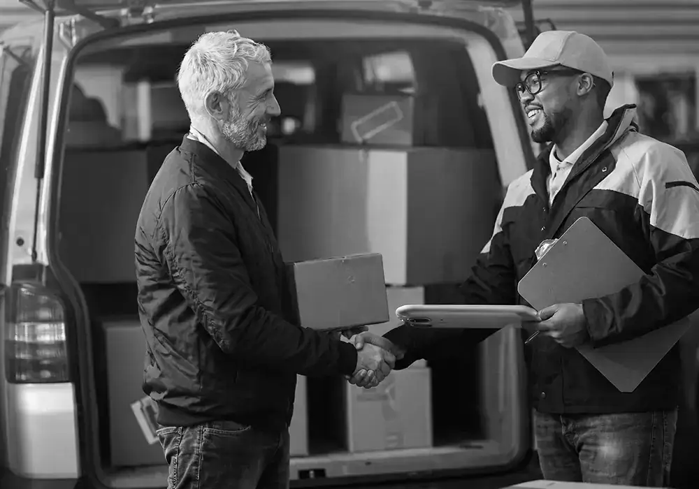 Livreur et client se serrant la main devant un véhicule utilitaire rempli de colis, illustrant la futur formation le transport de marchandises
