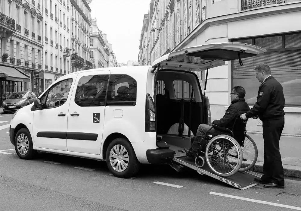 Chauffeur aidant une personne en fauteuil roulant à monter dans un véhicule adapté, illustrant la futur formation le transport de personnes à mobilité réduite
